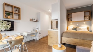 Una camera da letto moderna e compatta con un letto, un comodino e un angolo studio.