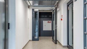 Un corridoio con porte contrassegnate con i numeri 1201-1205, un allarme antincendio e un cartello di uscita di sicurezza ben visibile.