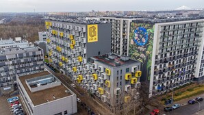 Un moderno edificio residenziale con un logo giallo distintivo, un giardino pensile e un murale sulla facciata.