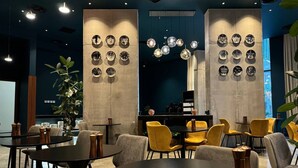Un interior moderno con mesas redondas, sillas amarillas, una planta grande y una pared decorada con platos circulares.