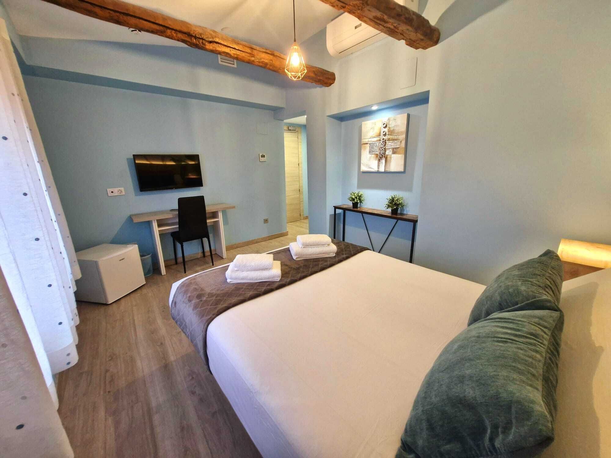 A hotel room with a bed, a desk, a chair, a TV, and a small table with plants.