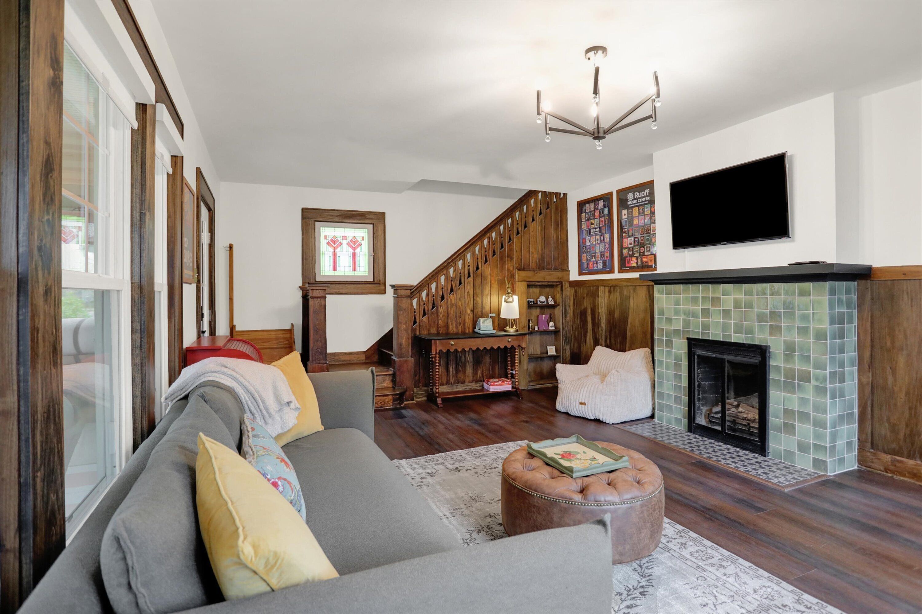Ein gemütliches Wohnzimmer mit Sofa, Hocker, Kamin und einer Holztreppe.