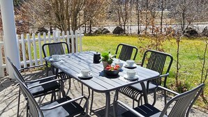 Een terras buiten met een tafel en stoelen, een wit hek en een uitzicht op een wijngaard en heuvels op de achtergrond.