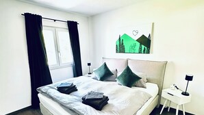 A neatly made bed with pillows and folded towels, a bedside table with a lamp, and a painting on the wall. - Forest Soul (Feldberg) - Terrace (Feldberg (Schwarzwald))