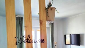A modern living room with a wooden accent wall, a welcoming sign, a television, and a small cabinet. - Cocooning apartment Air-conditioning / near center / Parking (Hyères)