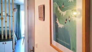 A hallway with a wooden slatted partition, a framed artwork depicting a wave and birds, and a door with a small wooden plaque. - Cocooning apartment Air-conditioning / near center / Parking (Hyères)