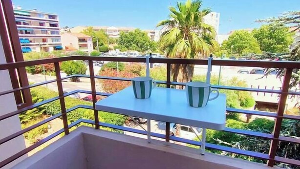 A balcony with two white chairs and a table, overlooking a residential area with buildings and palm trees. - Cocooning apartment Air-conditioning / near center / Parking (Hyères)