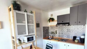 A compact kitchen with a wooden table and chairs, a microwave, a sink, and a patterned backsplash. - Cocooning apartment Air-conditioning / near center / Parking (Hyères)