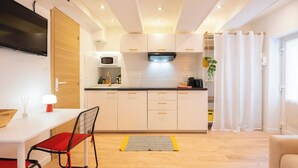 A modern kitchen with white cabinets, a black countertop, and a microwave. There is a dining area with a table and chairs, and a living room with a sofa. - Cocooning apartment near the sea (Carqueiranne)