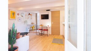 A modern living room with a dining area, a TV mounted on the wall, and a wooden door. - Cocooning apartment near the sea (Carqueiranne)