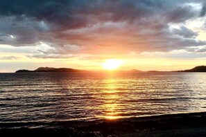 Un coucher de soleil sur une mer calme, avec des reliefs terrestres visibles au loin.