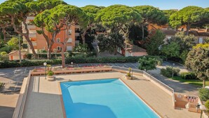 A rectangular pool with a tiled deck, surrounded by trees and a building with balconies. - Le toit du Port : Terraces/Pool/Clim/Parking (Hyères)