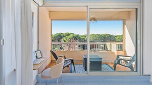 A balcony with a view of greenery and buildings, a desk with a laptop, and two chairs. - Le toit du Port : Terraces/Pool/Clim/Parking (Hyères)
