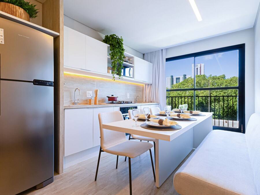 Una cocina moderna con refrigerador empotrado, muebles blancos y un comedor con mesa y sillas blancas.