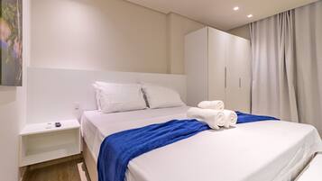 A modern hotel room with a large bed, a nightstand, a wardrobe, and a painting on the wall.