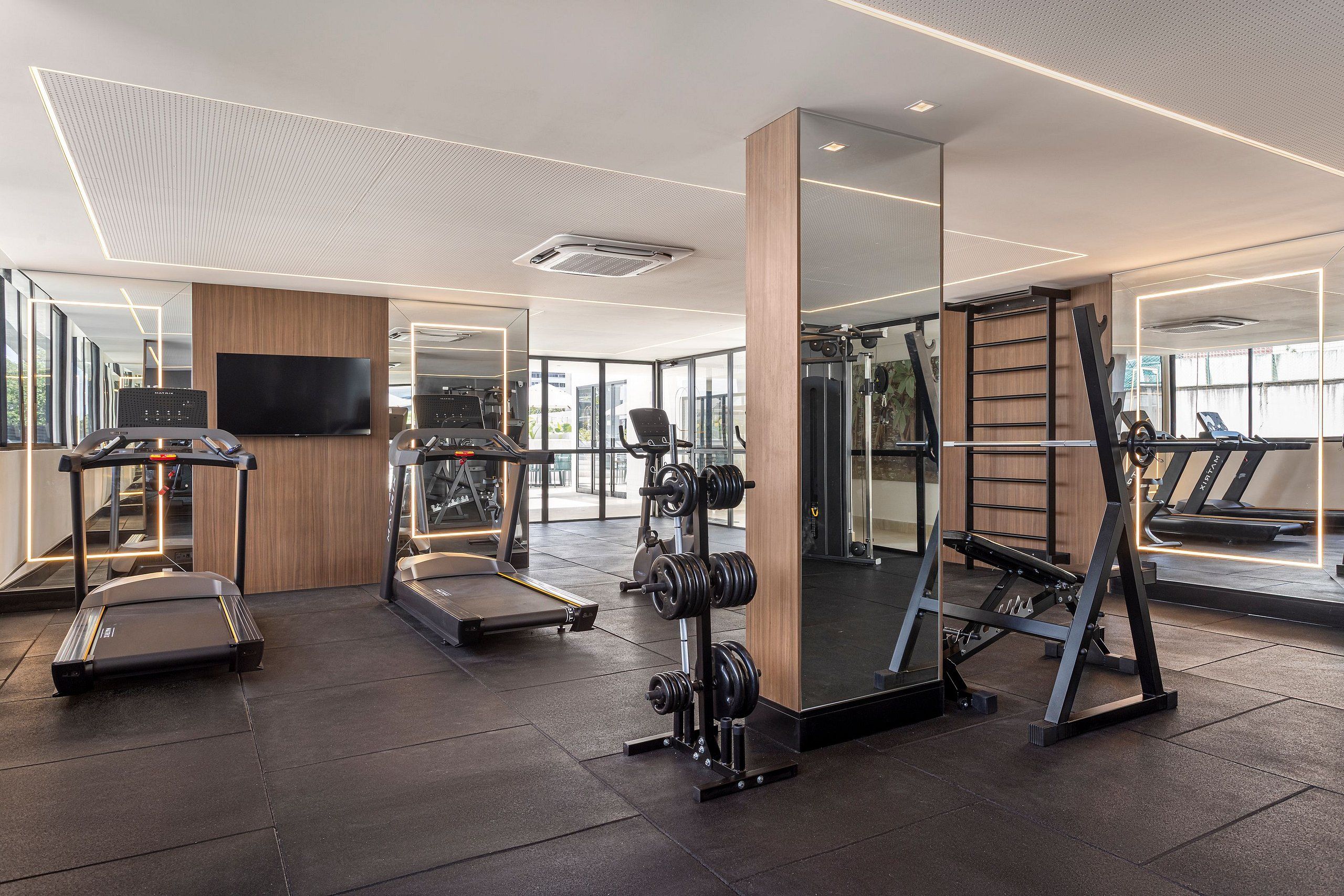 A modern gym with treadmills, a weight bench, and a mirrored wall.