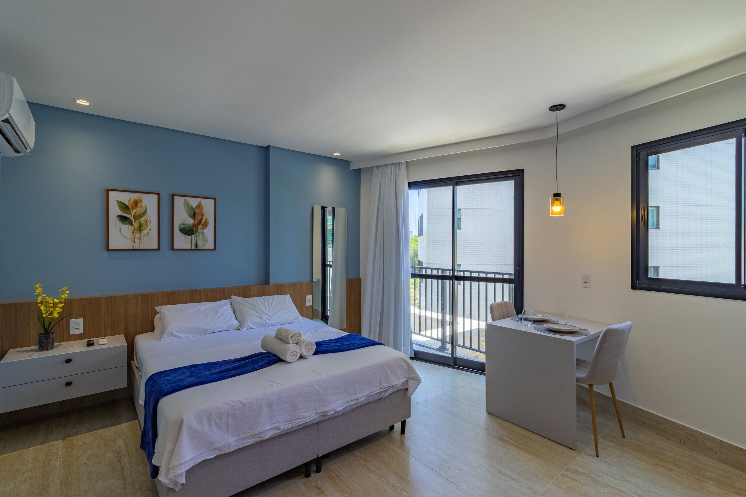 Habitación de hotel moderna con cama, escritorio y silla. Tiene un balcón con vista a edificios.