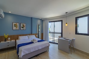 Habitación de hotel moderna con cama, escritorio y silla. Tiene un balcón con vista a edificios.