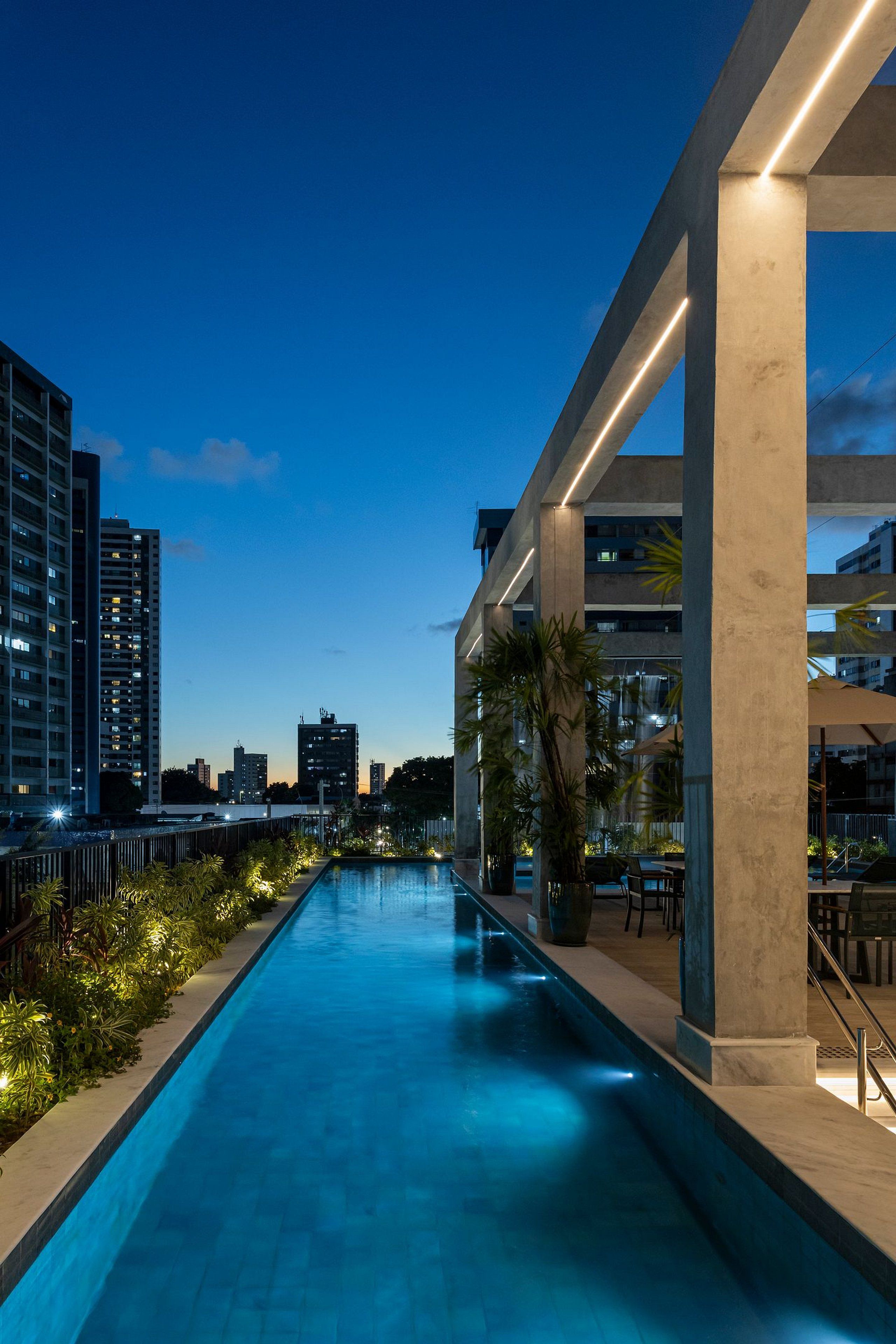 A swimming pool with a cityscape view, surrounded by modern buildings and palm trees.