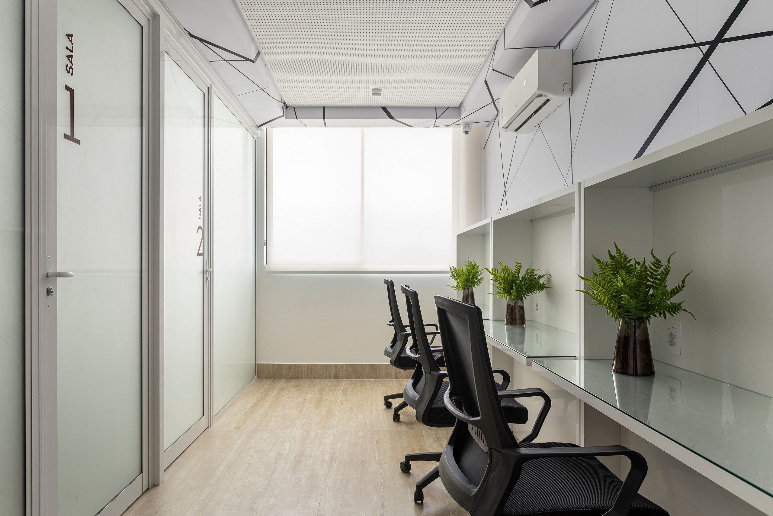 A conference room with glass walls, a white ceiling, and a large window. There are black office chairs and potted plants on the glass table.