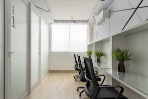 Un salón de conferencias con paredes de vidrio, techo blanco y un ventanal grande. Hay sillas de oficina negras y plantas en macetas sobre la mesa de vidrio.