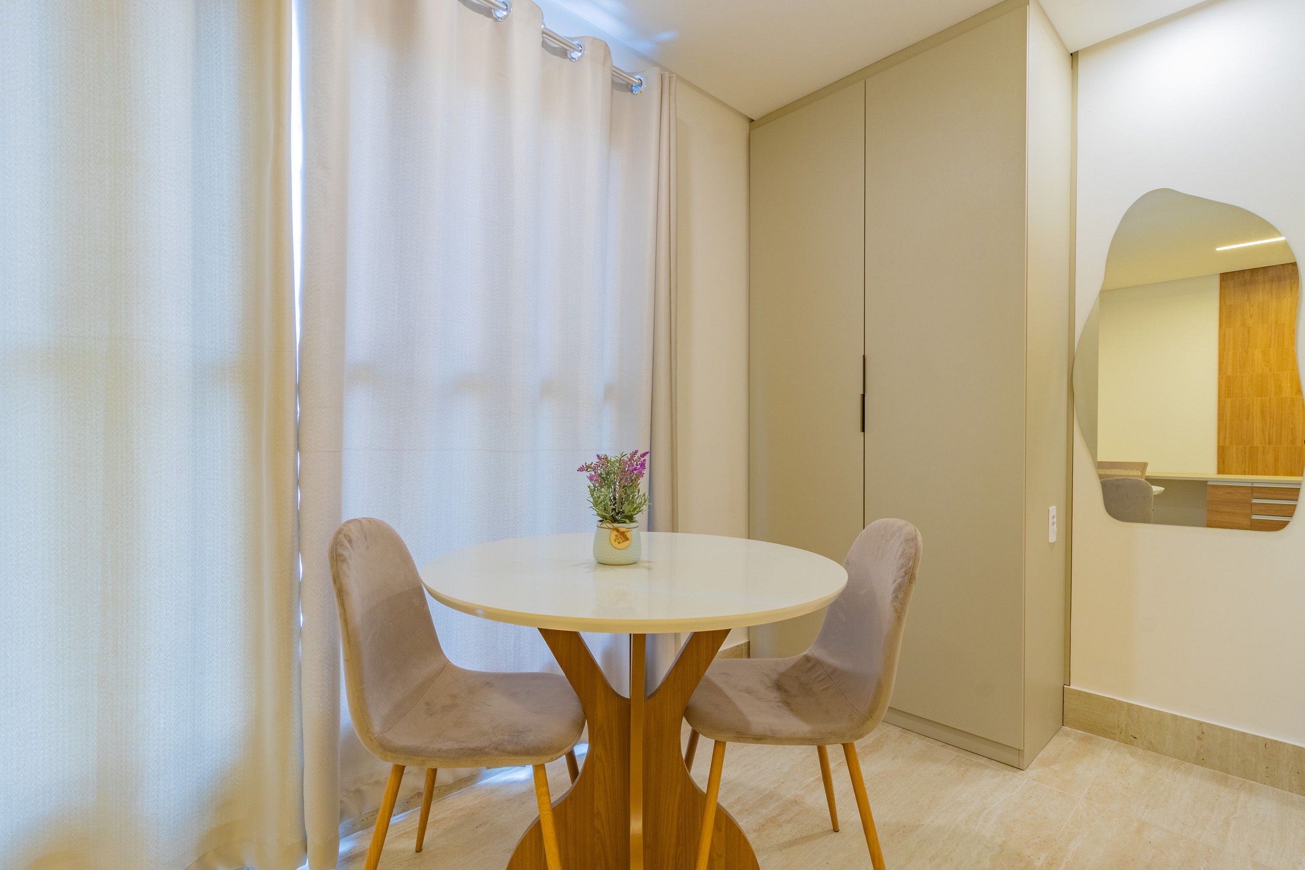 Una habitación moderna con una mesa redonda, dos sillas, un florero con flores y un espejo en la pared.