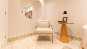 A modern room with a round mirror, a small wooden table with a lamp, and a cushioned chair. - Riverside HOUSI by Carpediem em Recife (Recife)