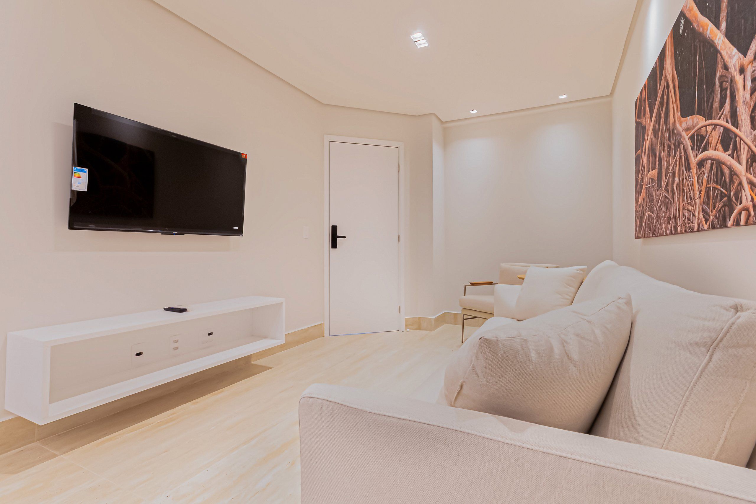 A modern living room with a flat-screen TV mounted on the wall, a white sofa, and a minimalist design.