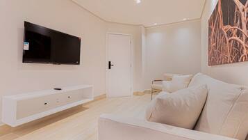 A modern living room with a flat-screen TV mounted on the wall, a white sofa, and a minimalist design.