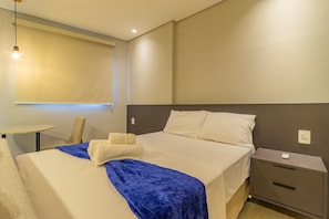 Una habitación de hotel ordenada con una cama, mesita de noche y una silla.