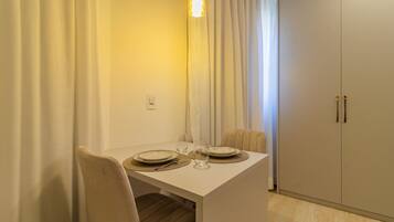 Un comedor con una mesa blanca dispuesta para dos, un colgador de luz y un armario de dos puertas.