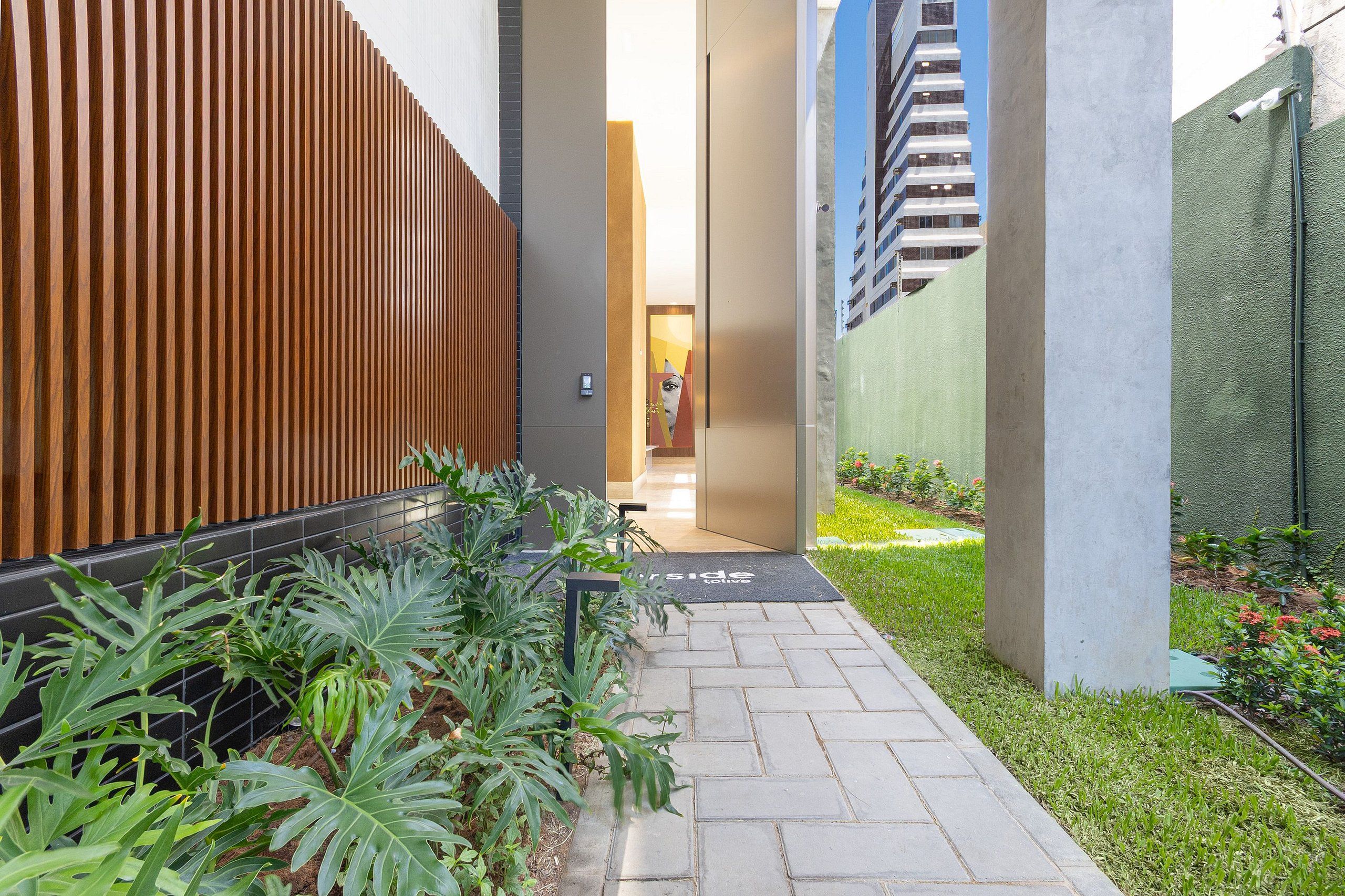 Un sendero que lleva a la entrada de un edificio, con una valla de madera, un pilar de concreto y una pared verde.
