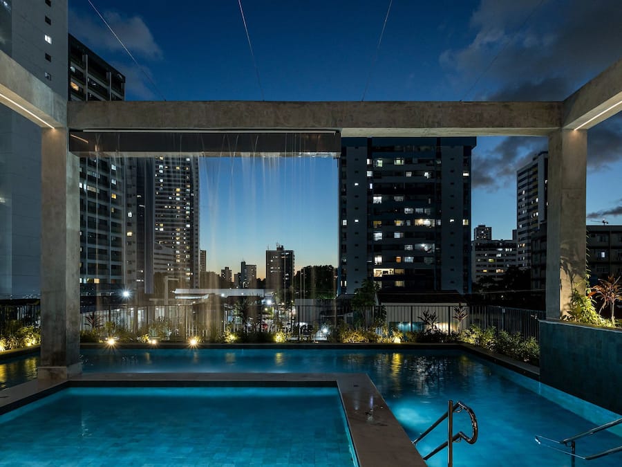 Una piscina exterior con vistas a un paisaje urbano, rodeada de edificios altos e iluminada por luces artificiales.
