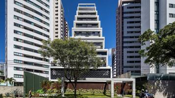 Um edifício moderno com vários andares, grandes janelas e área verde com árvores.