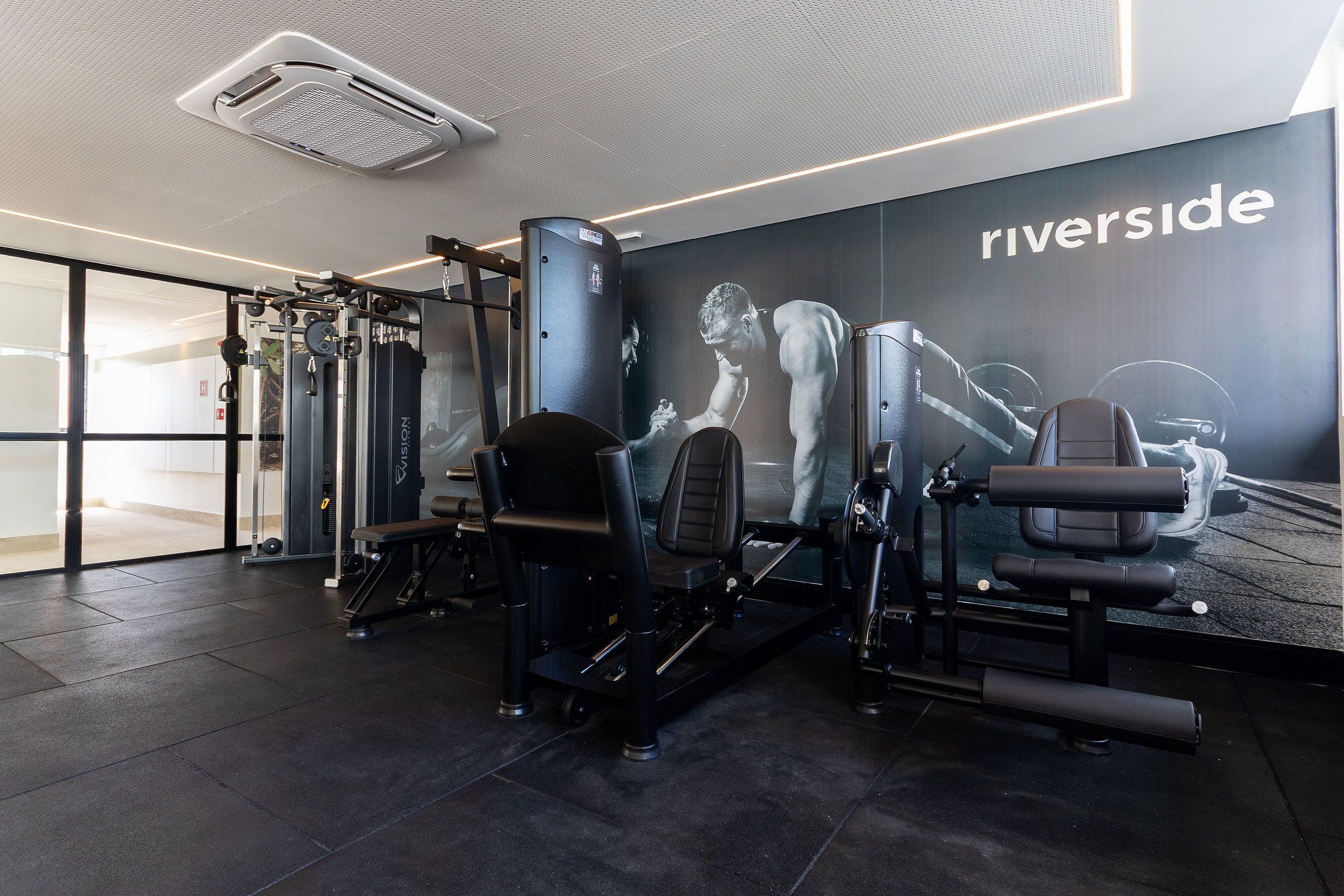 Une salle de sport moderne équipée de machines de musculation, d’un banc de développé couché et d’une grande affiche représentant un homme soulevant des poids.