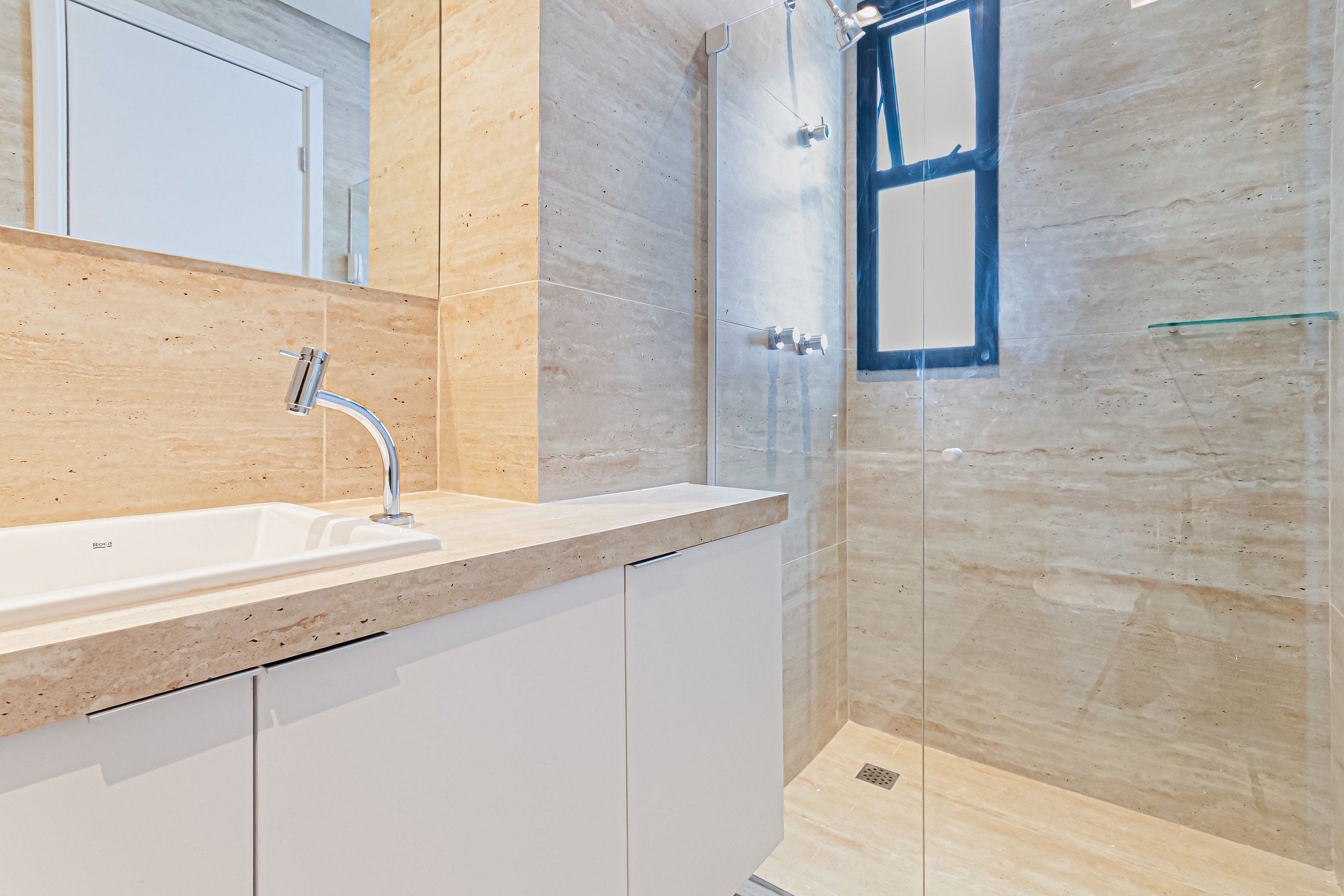Un baño moderno con cabina de ducha de vidrio, un lavamanos con grifo cromado y muebles de color blanco.