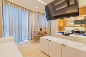 A modern hotel room with a flat-screen TV, a dining area with a table and chairs, and a bed with a TV on the headboard. - Riverside HOUSI by Carpediem em Recife (Recife)