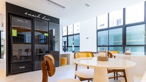 A modern interior with a round table and chairs, a black storefront with 'snack bar' signage, and large windows offering a view. - Riverside HOUSI by Carpediem em Recife (Recife)