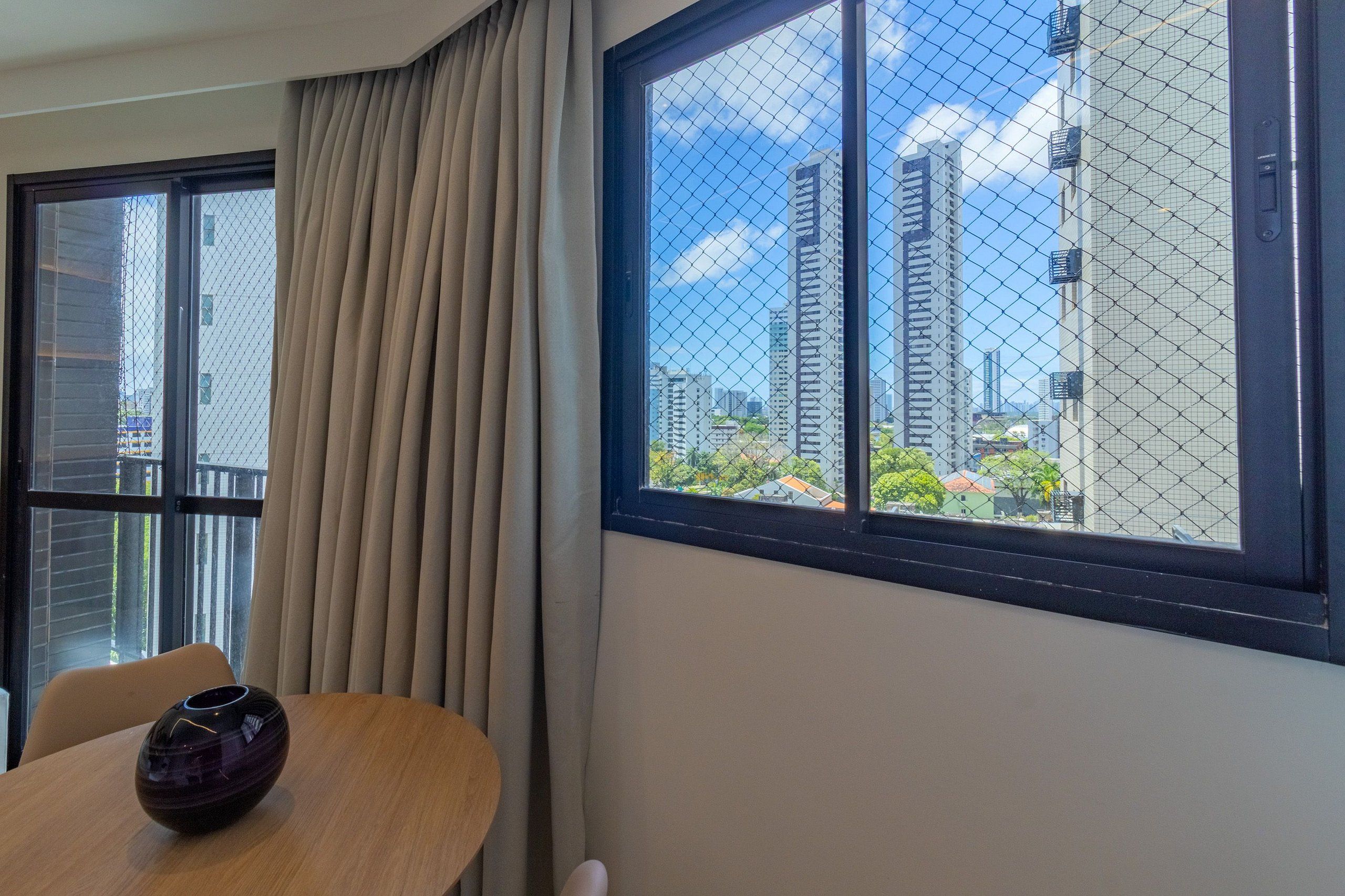A room with a view of tall buildings through a window with a mesh screen.