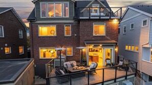 A two-story house with a balcony, a kitchen visible through the open door, and a patio area with outdoor furniture. - High-end city home loaded with amenities! (Seattle)