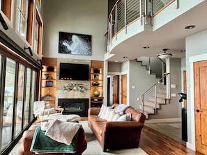 A spacious living room with a fireplace, a large TV mounted on the wall, and a staircase leading to an upper level. - Entire property: Main House, Bunk House  (separate) & Guest House (separate) (Friday Harbor)