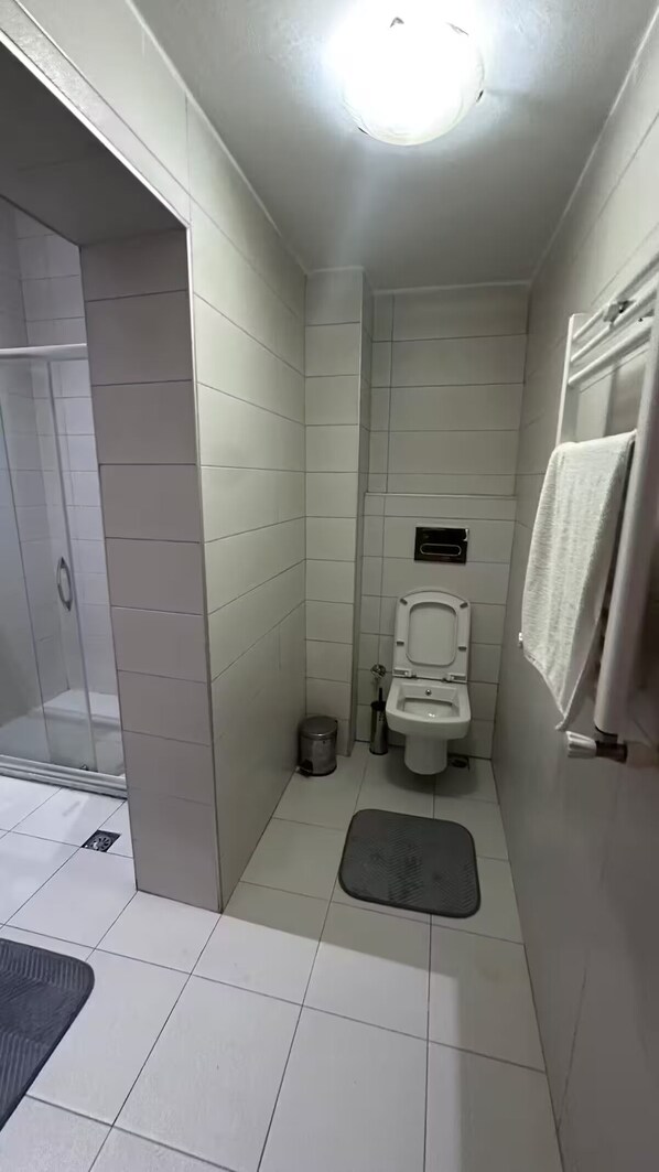 A small, tiled bathroom with a toilet, a shower area, and a towel rack.