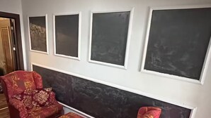 Una habitación con piso de madera oscura, un sofá rojo estampado, un sillón a juego y una pequeña mesa. Hay cuatro cuadros enmarcados en la pared.