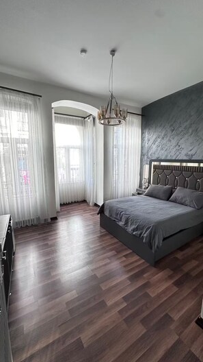 A modern bedroom with a large bed, wooden flooring, and a chandelier.