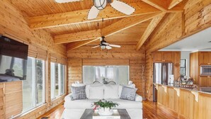 A cabin interior with a wooden ceiling, a white sofa, a coffee table, and a kitchen area.