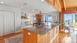 A spacious kitchen with a large island, wooden ceiling, and a view to the outside.