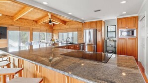 A spacious kitchen with a large island, wooden cabinets, stainless steel appliances, and a ceiling fan.