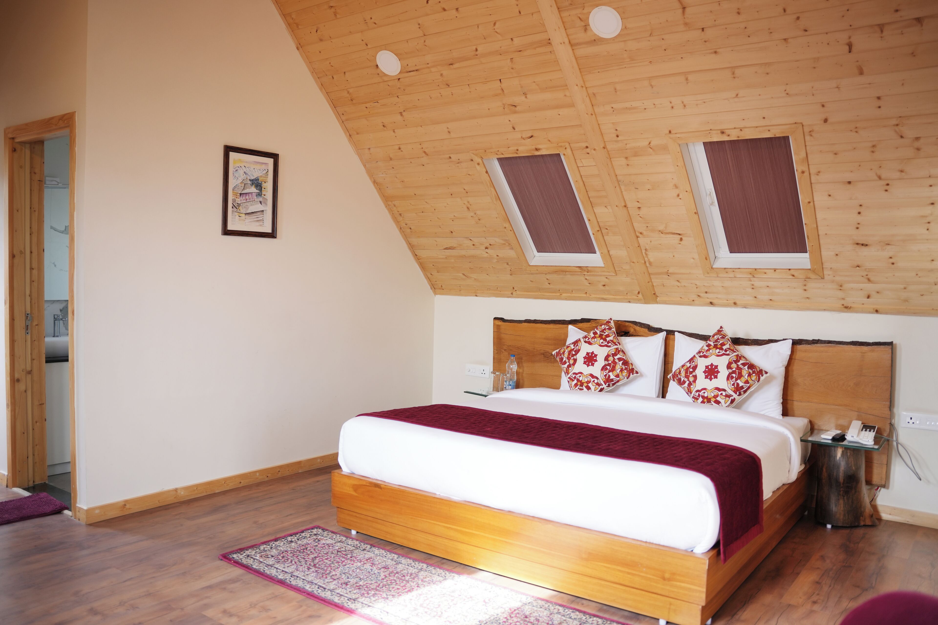 A bedroom with a wooden ceiling, a large bed with a red blanket, and a small bedside table.