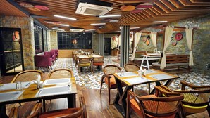 A restaurant with wooden flooring, wicker chairs, and tables set with white tablecloths. - Samsara Luxury Cottages & Spa  (Kandaghat)