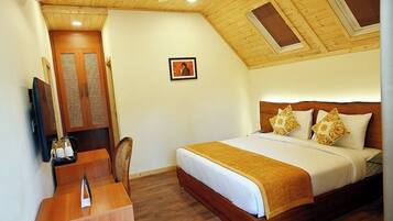 Une chambre d’hôtel avec un plafond en bois, un lit avec une literie blanche et dorée, un bureau en bois avec une chaise, et un tableau encadré accroché au mur.